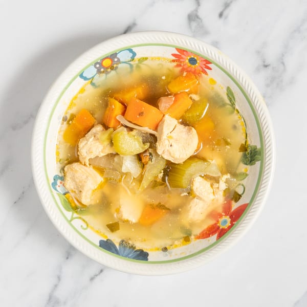Chicken and vegetable soup with carrots, celery, and onions in a floral bowl.