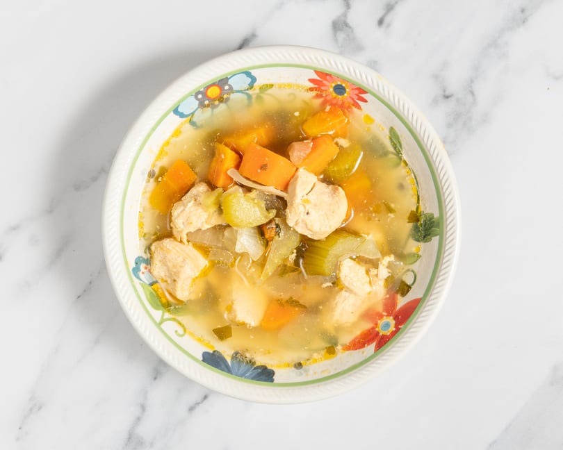 Chicken and vegetable soup with carrots, celery, and onions in a floral bowl.