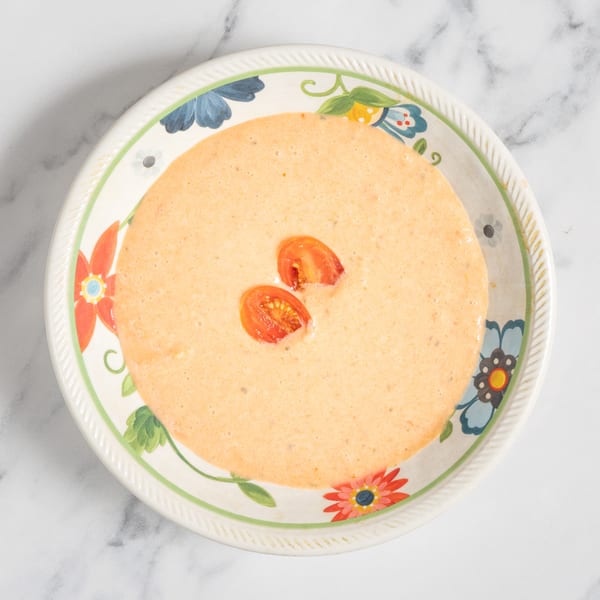 Creamy orange soup with two halved cherry tomatoes in a floral-patterned bowl.