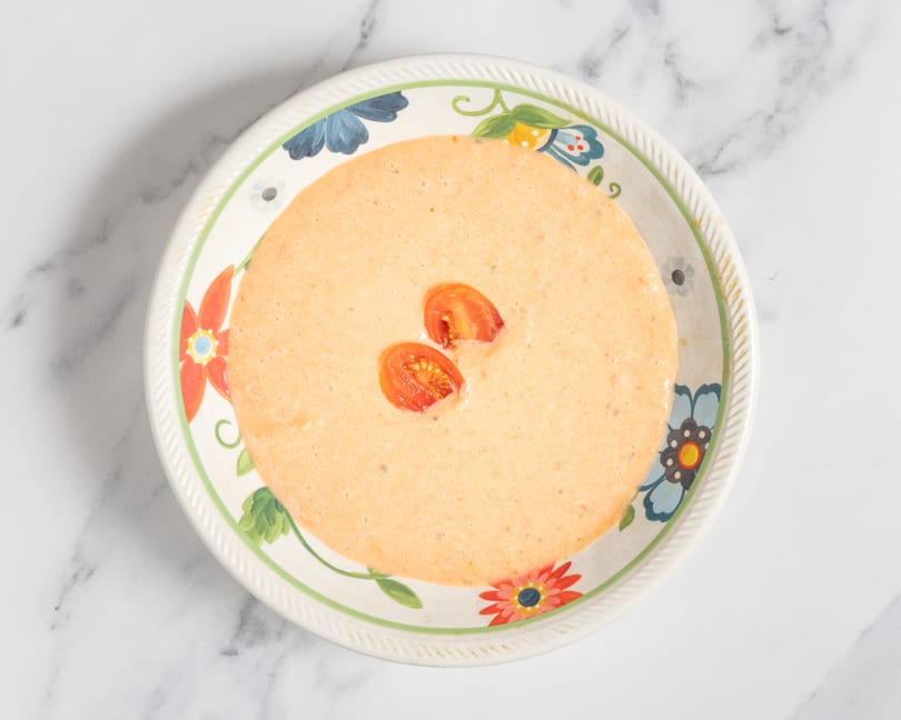 Creamy orange soup with two halved cherry tomatoes in a floral-patterned bowl.
