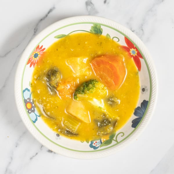 Overhead view of a colorful bowl filled with a hearty vegetable soup, featuring carrots, potatoes, and broccoli.