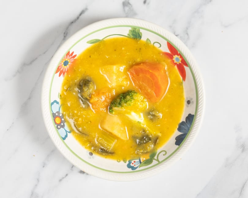 Overhead view of a colorful bowl filled with a hearty vegetable soup, featuring carrots, potatoes, and broccoli.