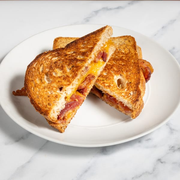 Grilled cheese sandwich with bacon, cut in half diagonally, on a white plate.