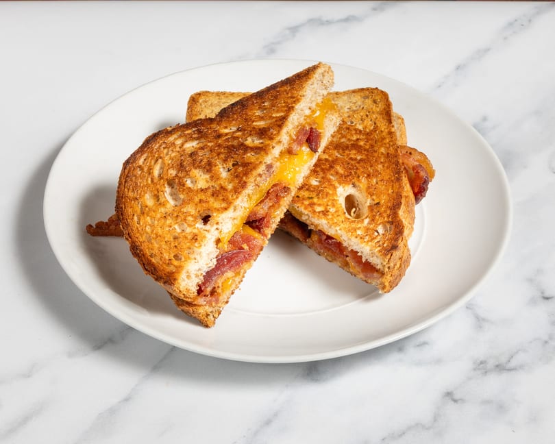 Grilled cheese sandwich with bacon, cut in half diagonally, on a white plate.