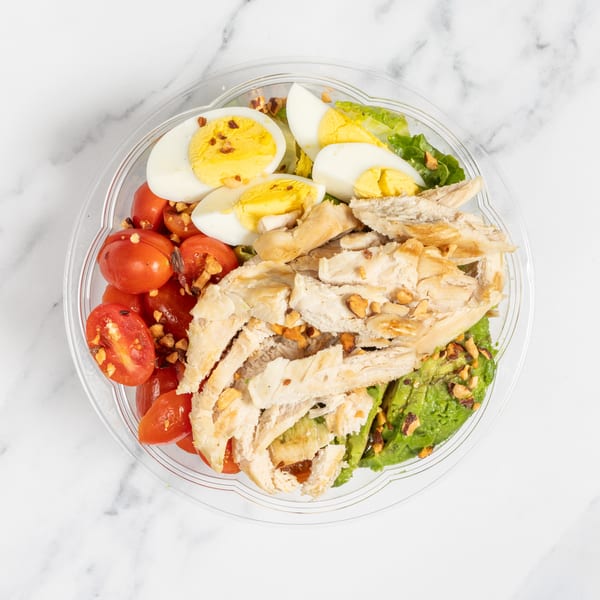 Overhead view of a salad with chicken, cherry tomatoes, hard-boiled eggs, and avocado.