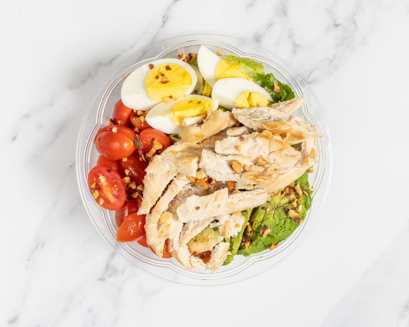 Overhead view of a salad with chicken, cherry tomatoes, hard-boiled eggs, and avocado.