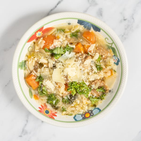 A colorful bowl of Italian wedding soup with pasta, meatballs, vegetables, and parmesan cheese.