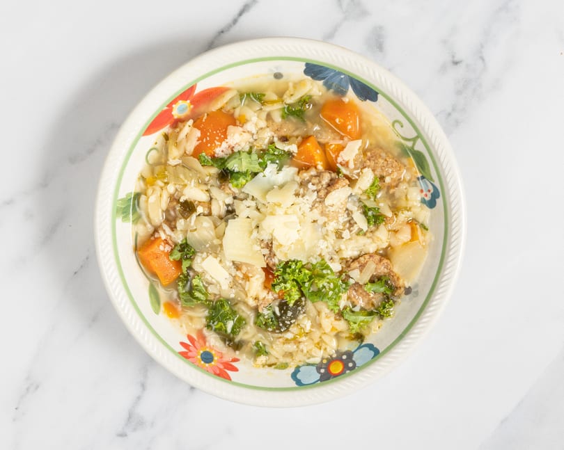 A colorful bowl of Italian wedding soup with pasta, meatballs, vegetables, and parmesan cheese.