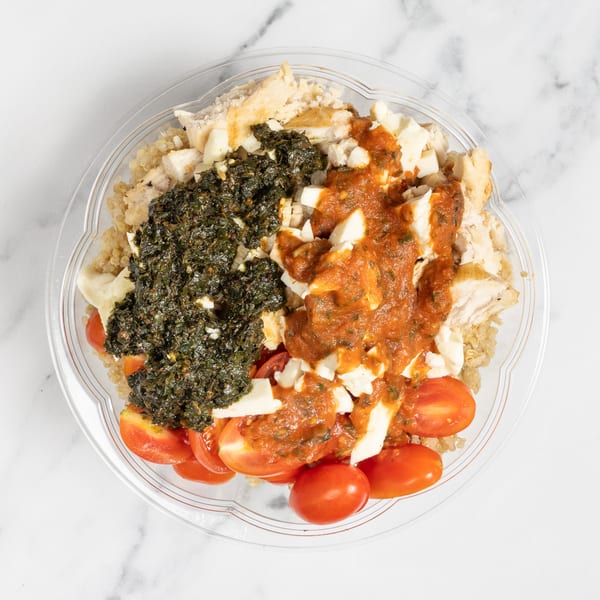 Overhead view of a chicken and quinoa bowl with pesto, tomato sauce, mozzarella, and cherry tomatoes.