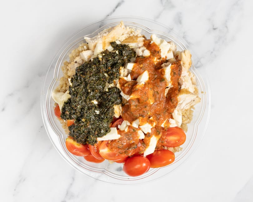 Overhead view of a chicken and quinoa bowl with pesto, tomato sauce, mozzarella, and cherry tomatoes.