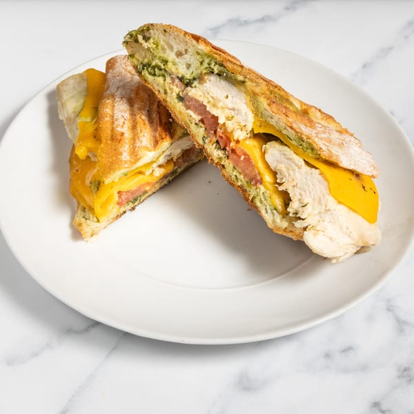 Two halves of a chicken panini with melted cheese, tomatoes, and pesto on a white plate.