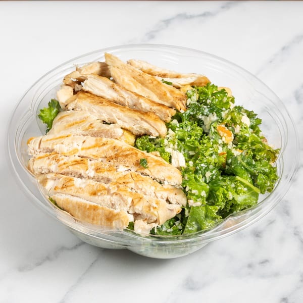 Grilled chicken strips and kale salad with dressing in a clear plastic container.