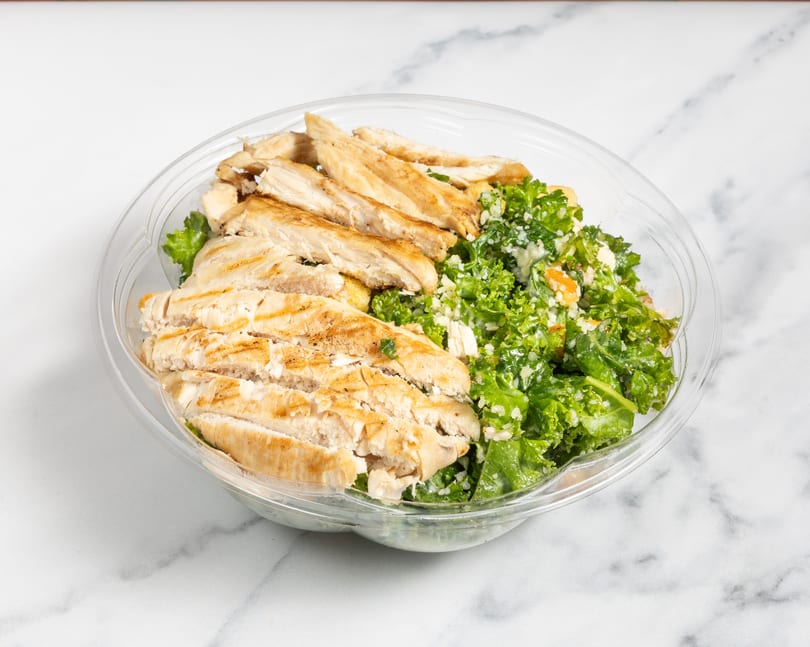 Grilled chicken strips and kale salad with dressing in a clear plastic container.