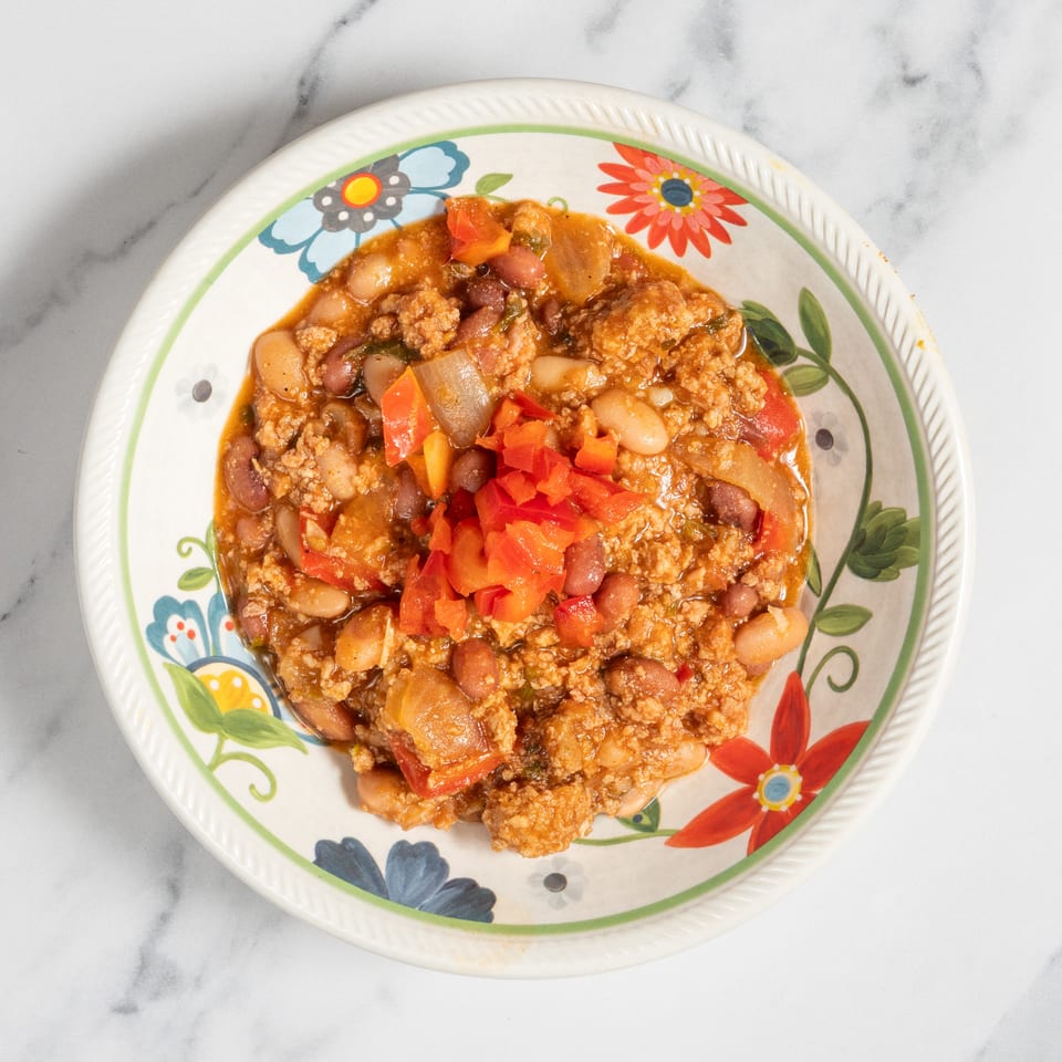 Hearty chili with ground meat, beans, and diced red peppers in a floral bowl on marble.