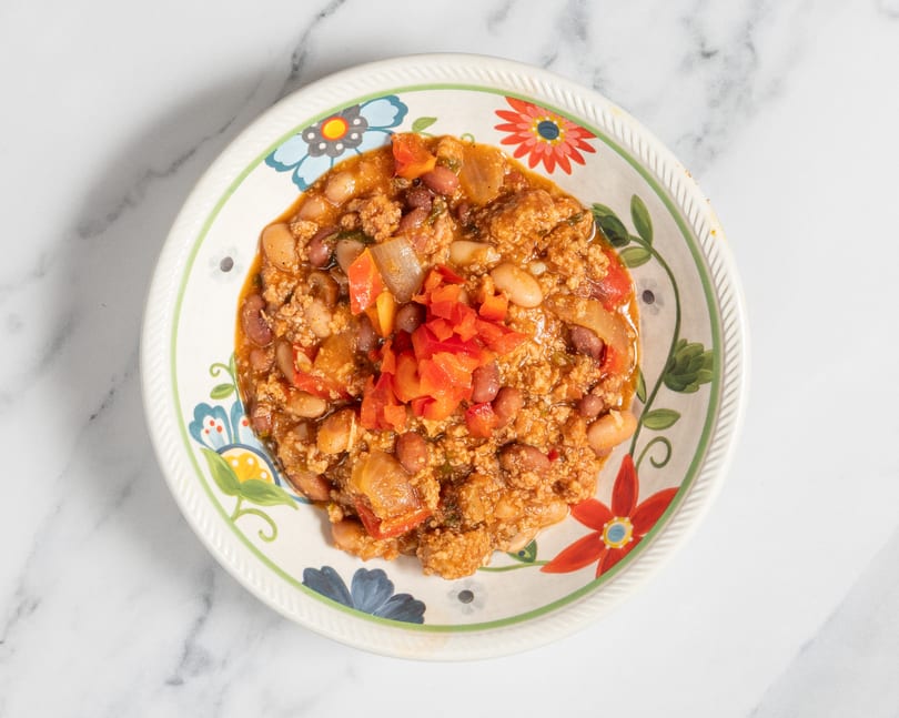 Hearty chili with ground meat, beans, and diced red peppers in a floral bowl on marble.